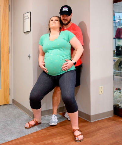 Husband supporting pregnant wife doing a wall squat 